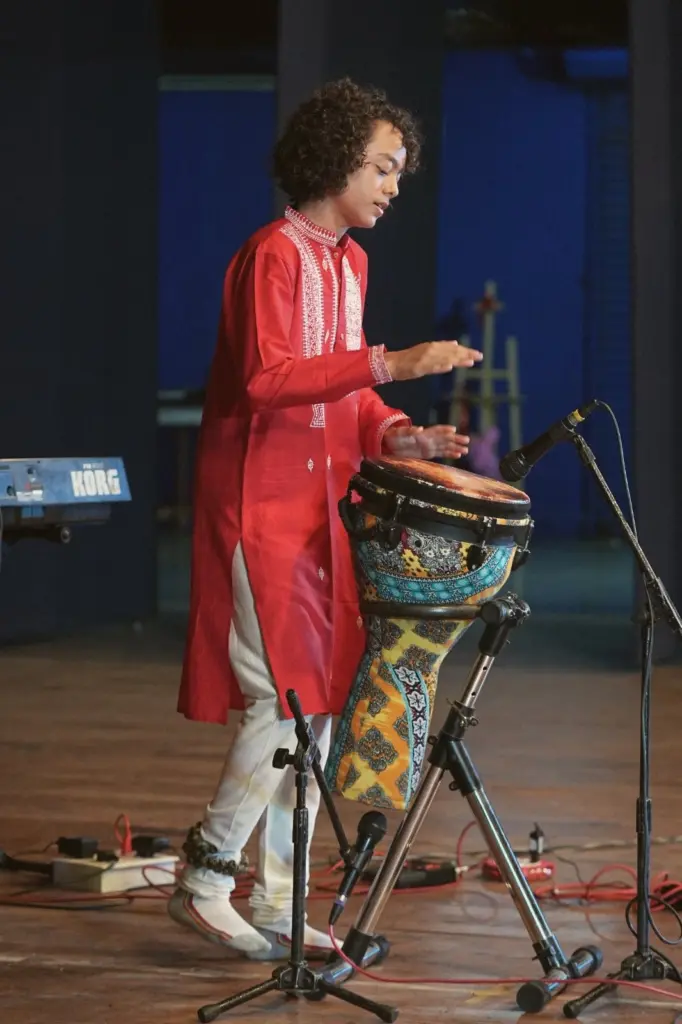 Aurum playing the djembe on stage in a red kurta