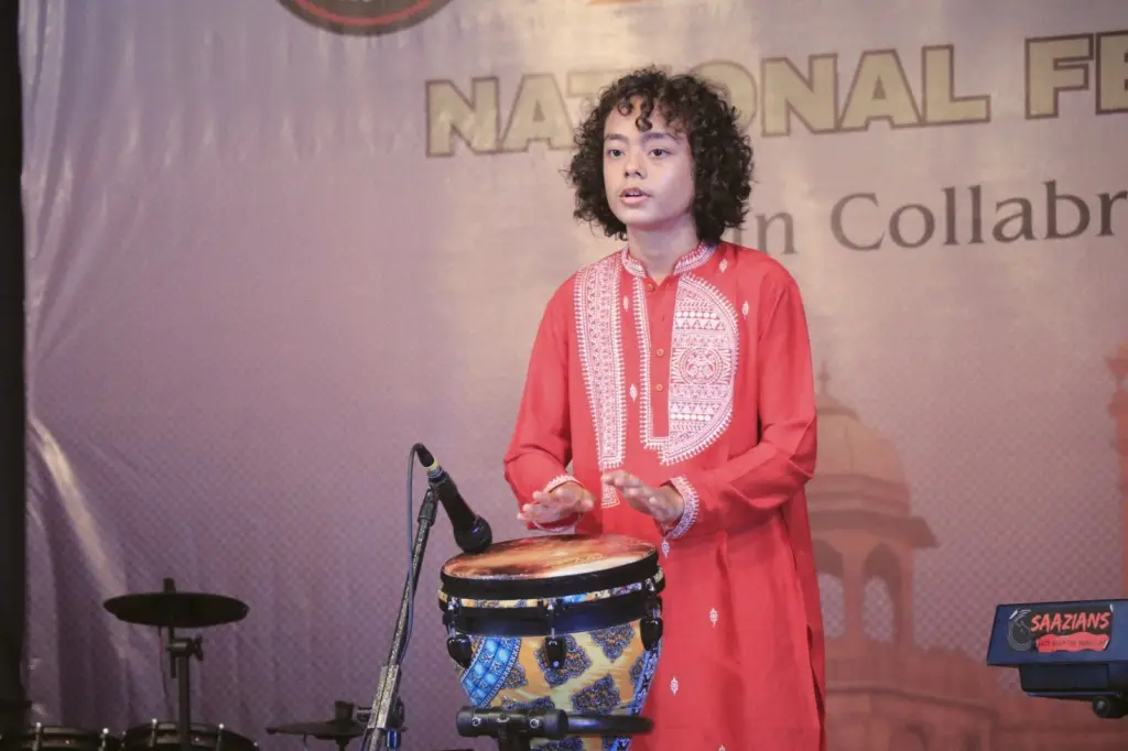Aurum playing the djembe in front of a festival backdrop